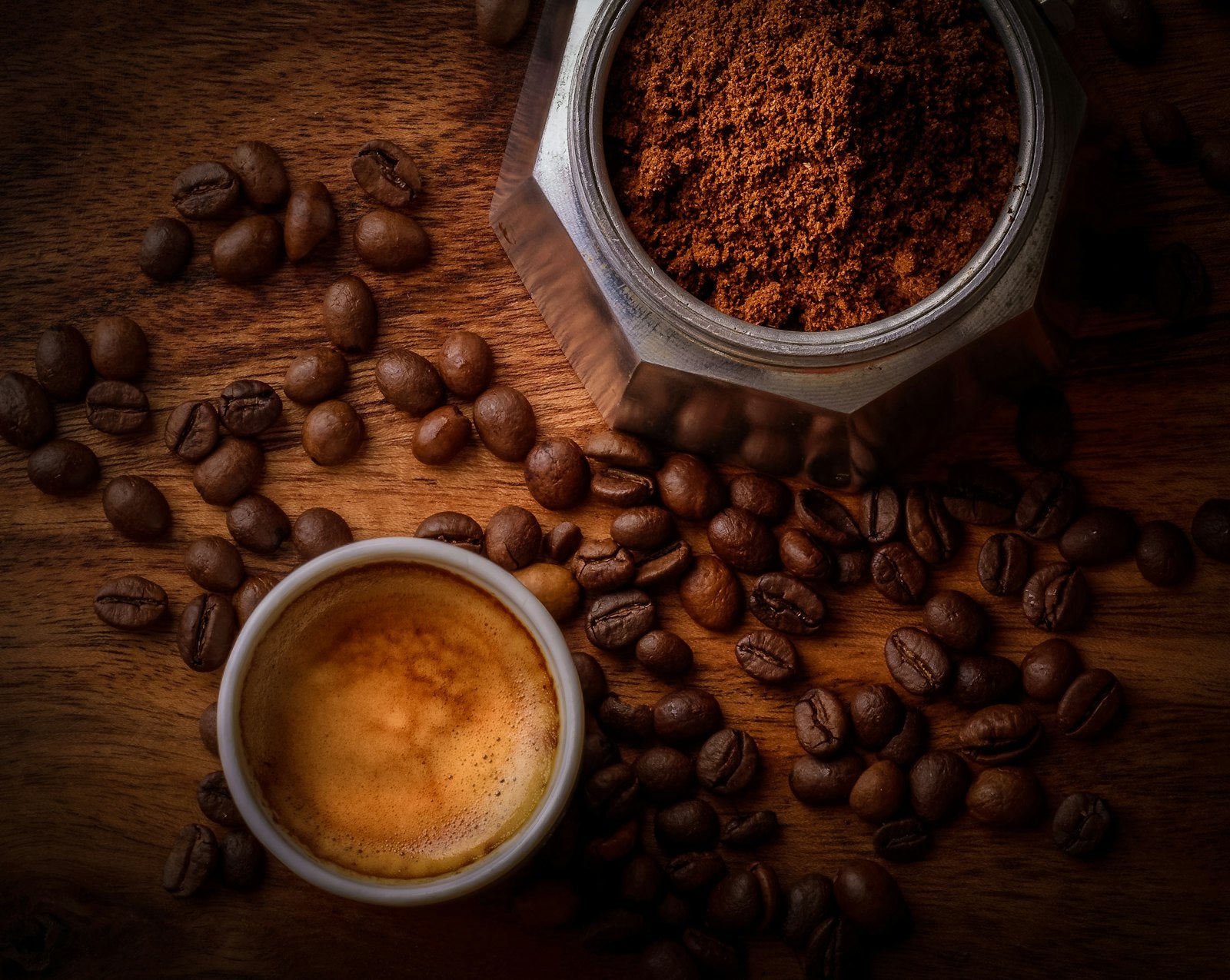 Espresso, scattered beans and a jar of ground coffee on a wooden table