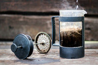 A French press brewing on a weathered wooden table