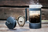 A French press brewing on a weathered wooden table