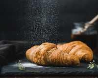 A croissant dusted with flour against a dark ground
