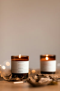 Two amber glass candle jars lit on a pale surface