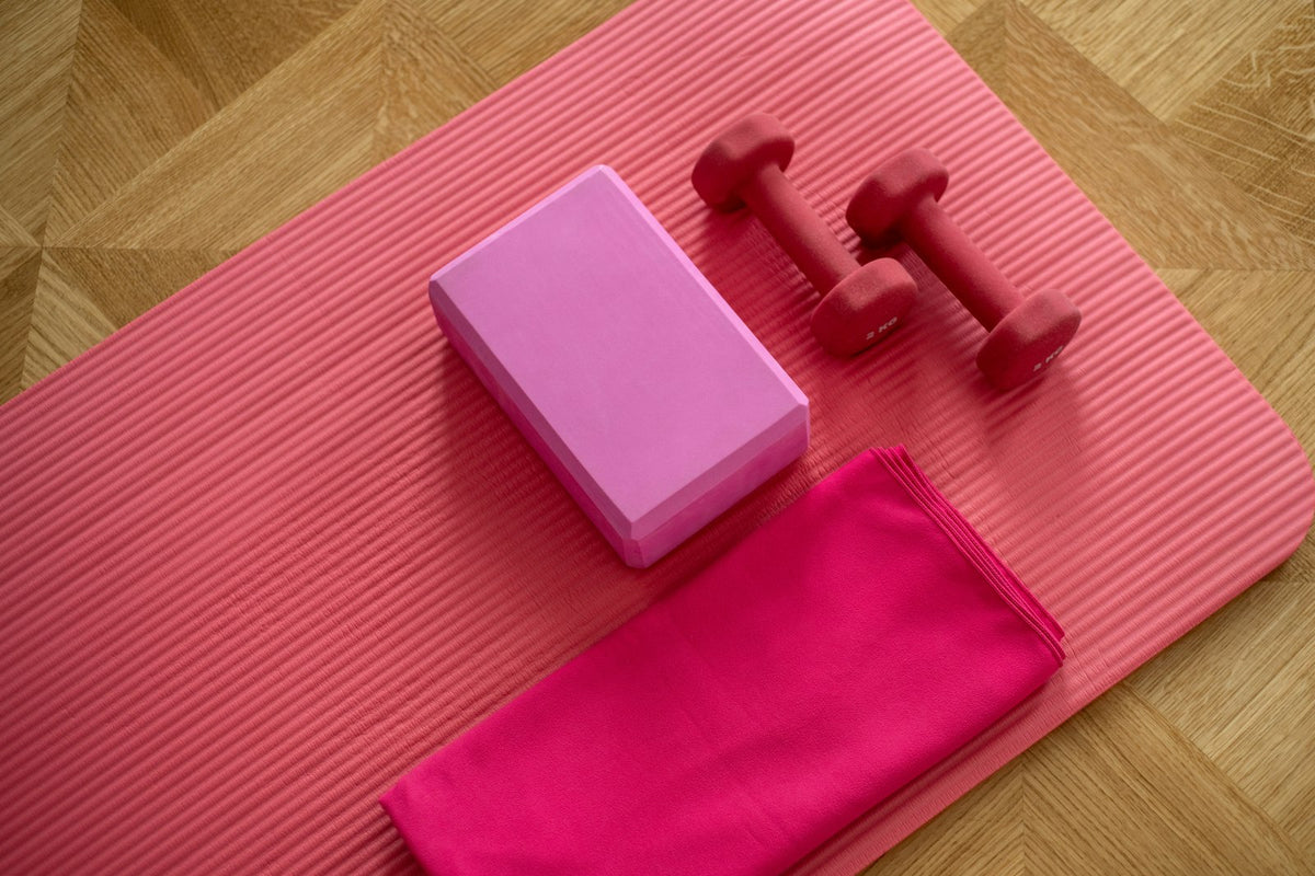 A foam yoga block and strap laid on a pink mat