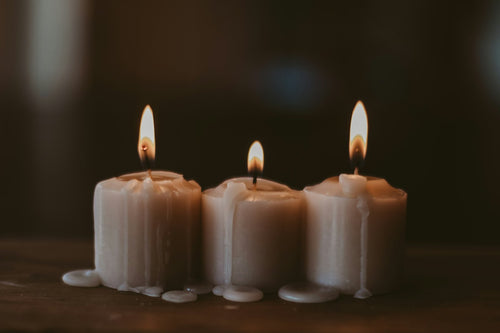 Three cream pillar candles burning against a dark ground