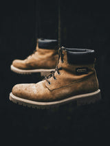 A tan suede work boot suspended against a dark background