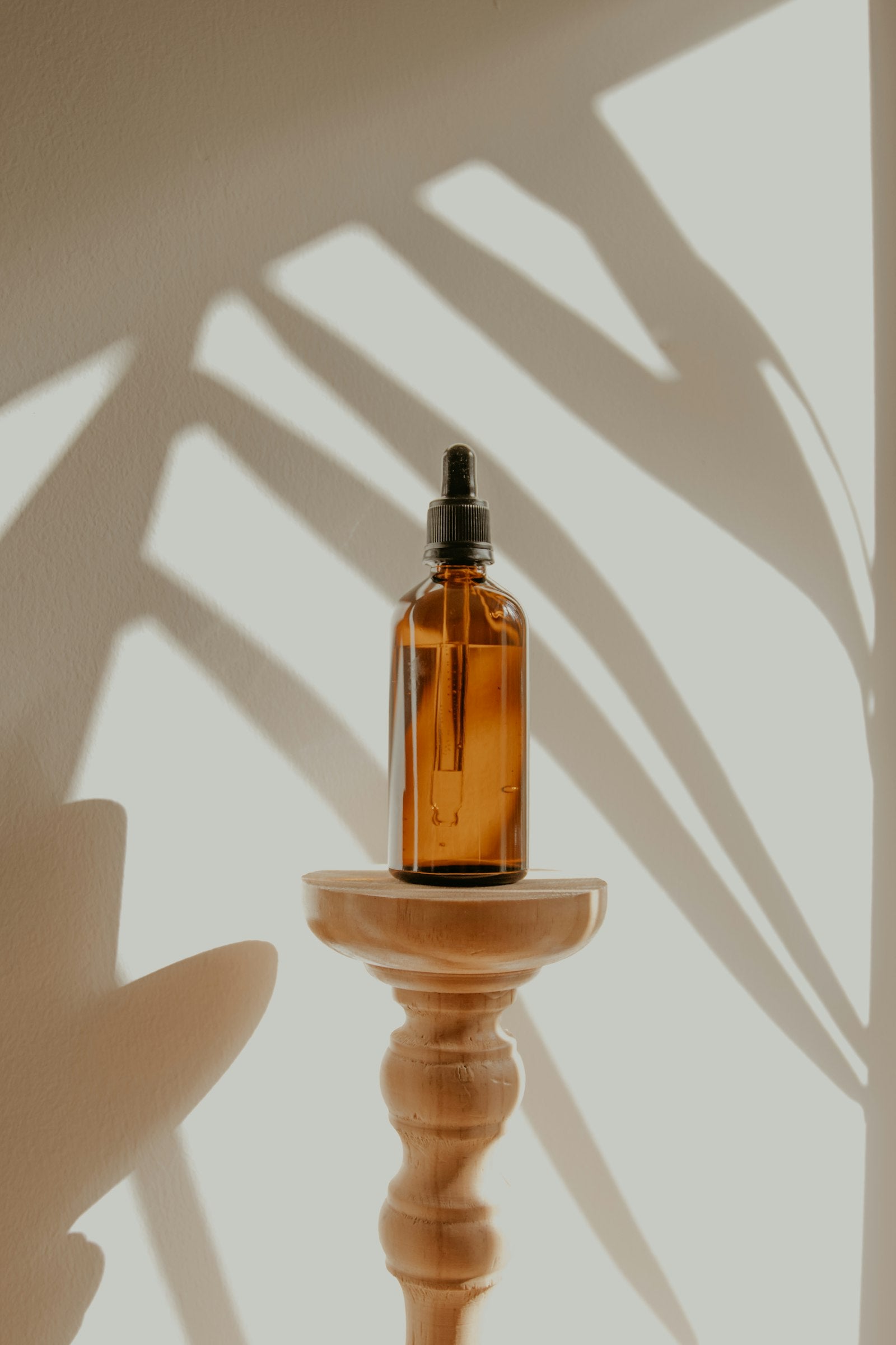 An amber dropper bottle on a wooden stand in palm shadow