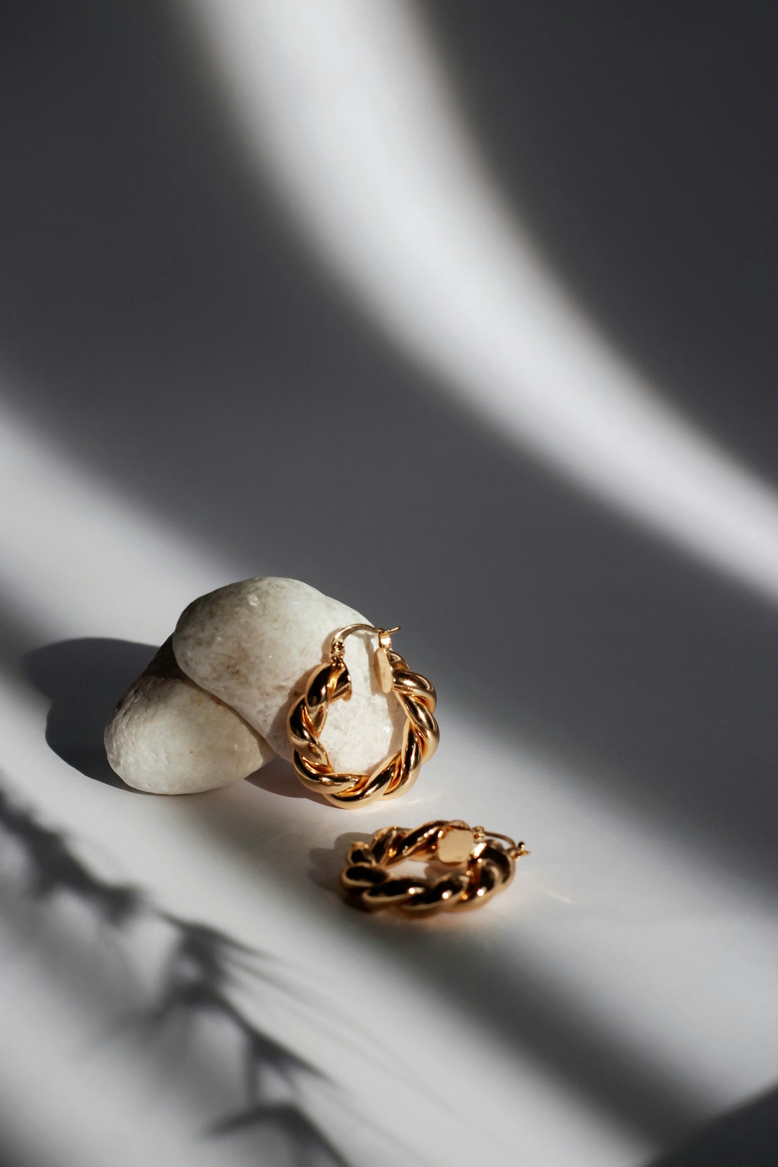 A pair of twisted gold hoop earrings resting on pale stones