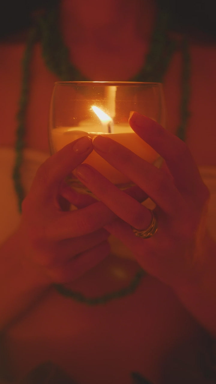Cupped hands holding a lit candle in a glass