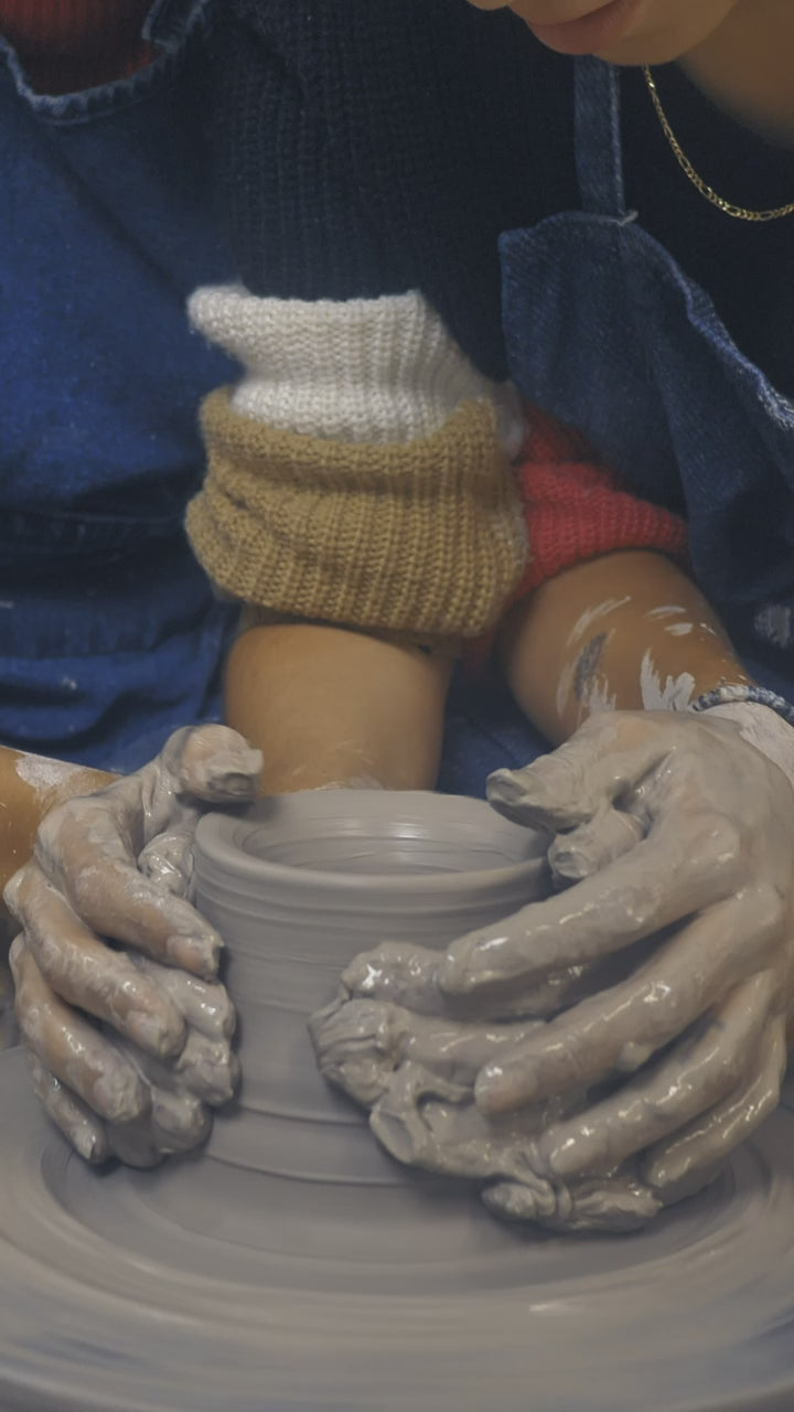 Two makers shaping a bowl together at the wheel