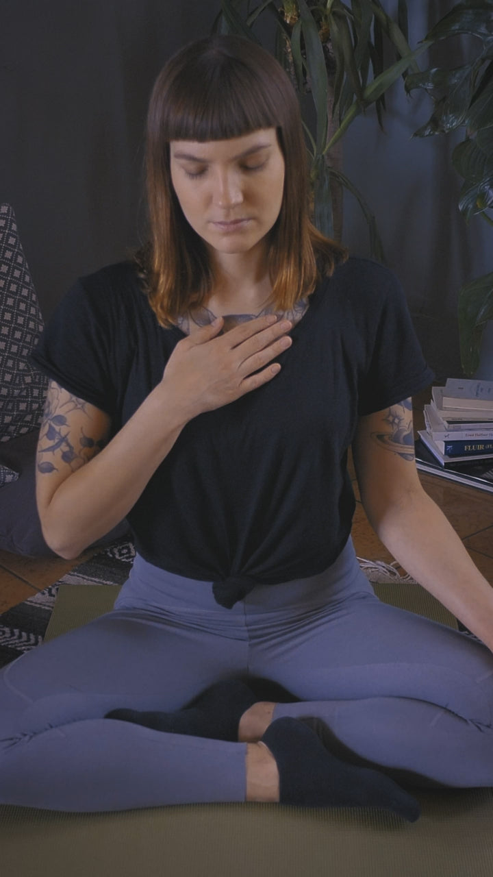 Seated cross-legged with a hand resting on the heart