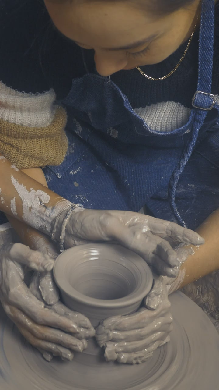Hands centring wet clay on a spinning potter's wheel