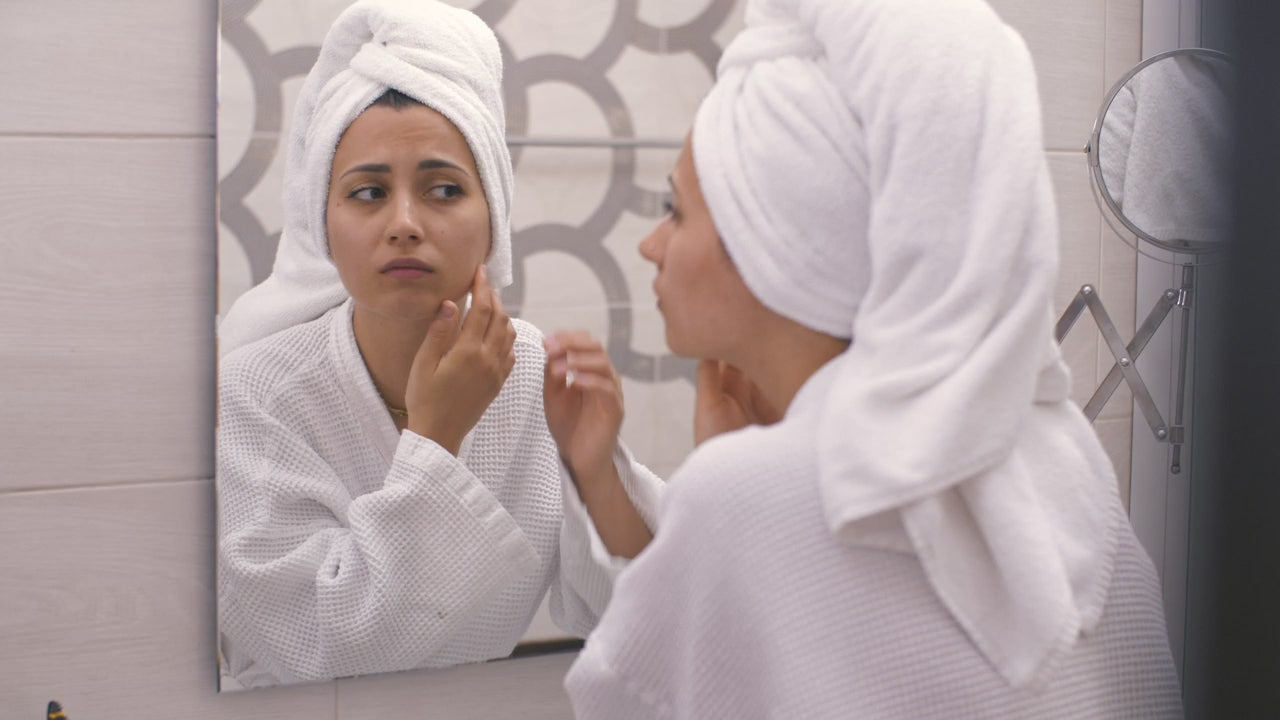 Applying product at a bathroom mirror in a towel wrap