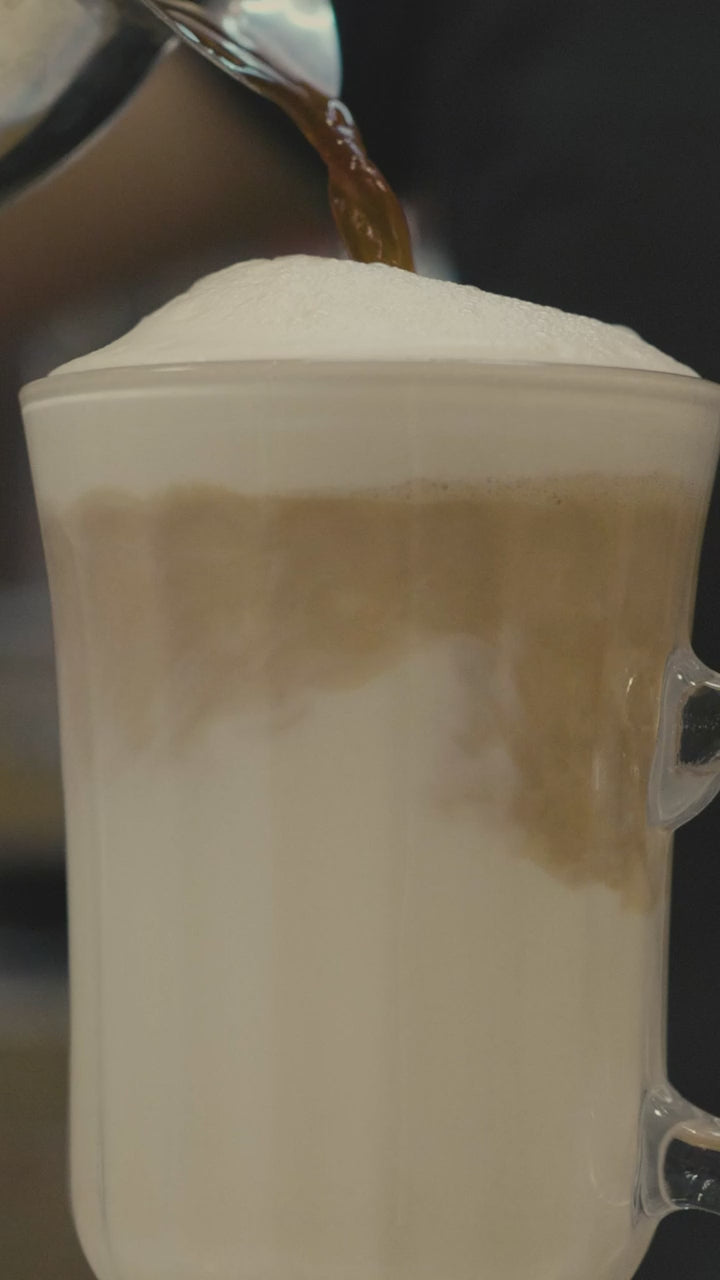 Milk poured into a tall glass of coffee, forming a layered latte